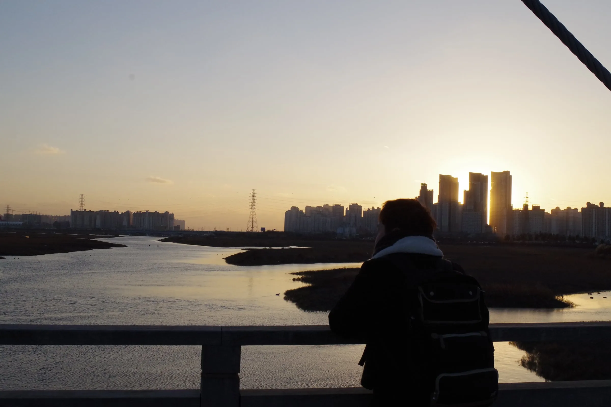 해 질 녘 물길과 아파트 숲, 다리 난간에 선 사람의 뒷모습